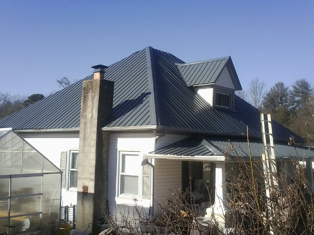 Dark blue standing seam metal roof on a white farmhouse with dormer — Slate & Tile Roof Repair by Roofing Brothers in Birmingham