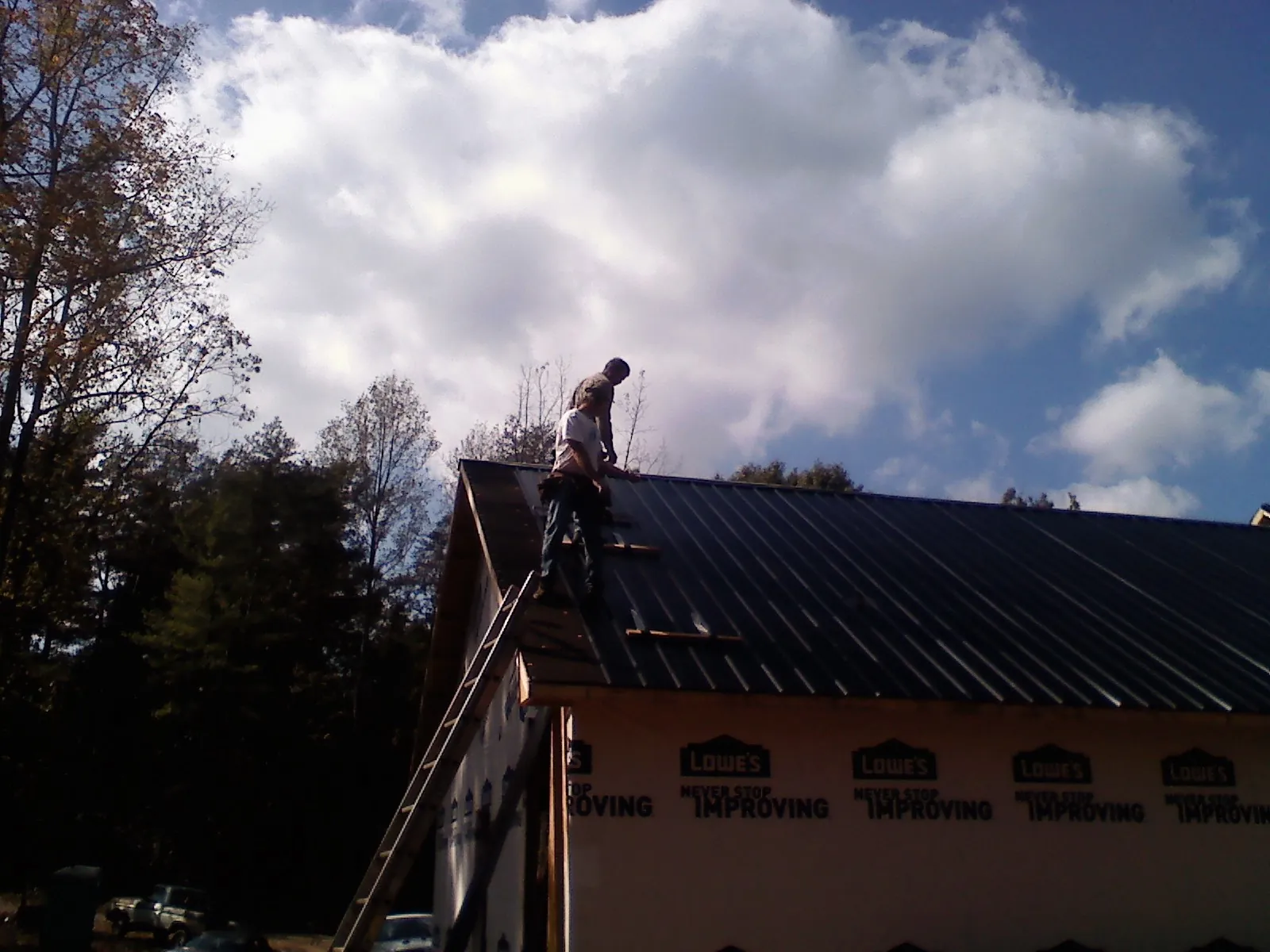 Roofer fastening dark metal panels high against a cloudy sky, from a Roof Inspection job in Birmingham